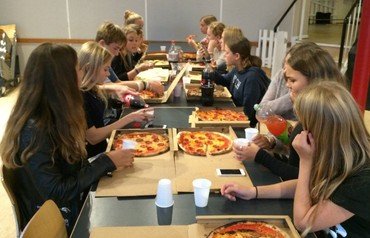 Konfirmander spiser pizza i KonfirmandCaféen siddende på begge sider af et langt bord