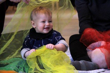 Smilende baby, der sidder og lege på gulvet med gult ciffontørklæde
