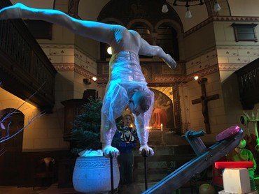 Cirkusartist i gennemsigtig plastikdragt står på hænder i kirken.