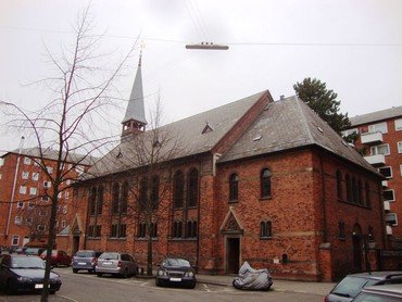 Sct. Lukas kirke fra siden ud mod Chr. Richardts Vej. Parkerede biler lang kirken. Træ og himmel i efterårsdragt